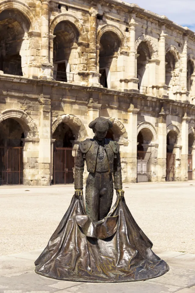 Statue von Nimeño II., mit der Arena von Nîmes im Hintergrund