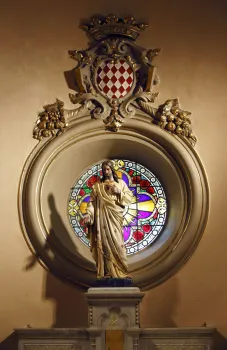 Kirche der Heiligen Devota, Jesus-Statue vor einem Rundfenster mit Ornamenten und Wappen